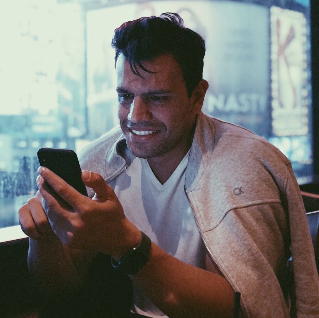 Daniel Malinoski sorrindo enquanto olha o celular, com luzes da cidade ao fundo